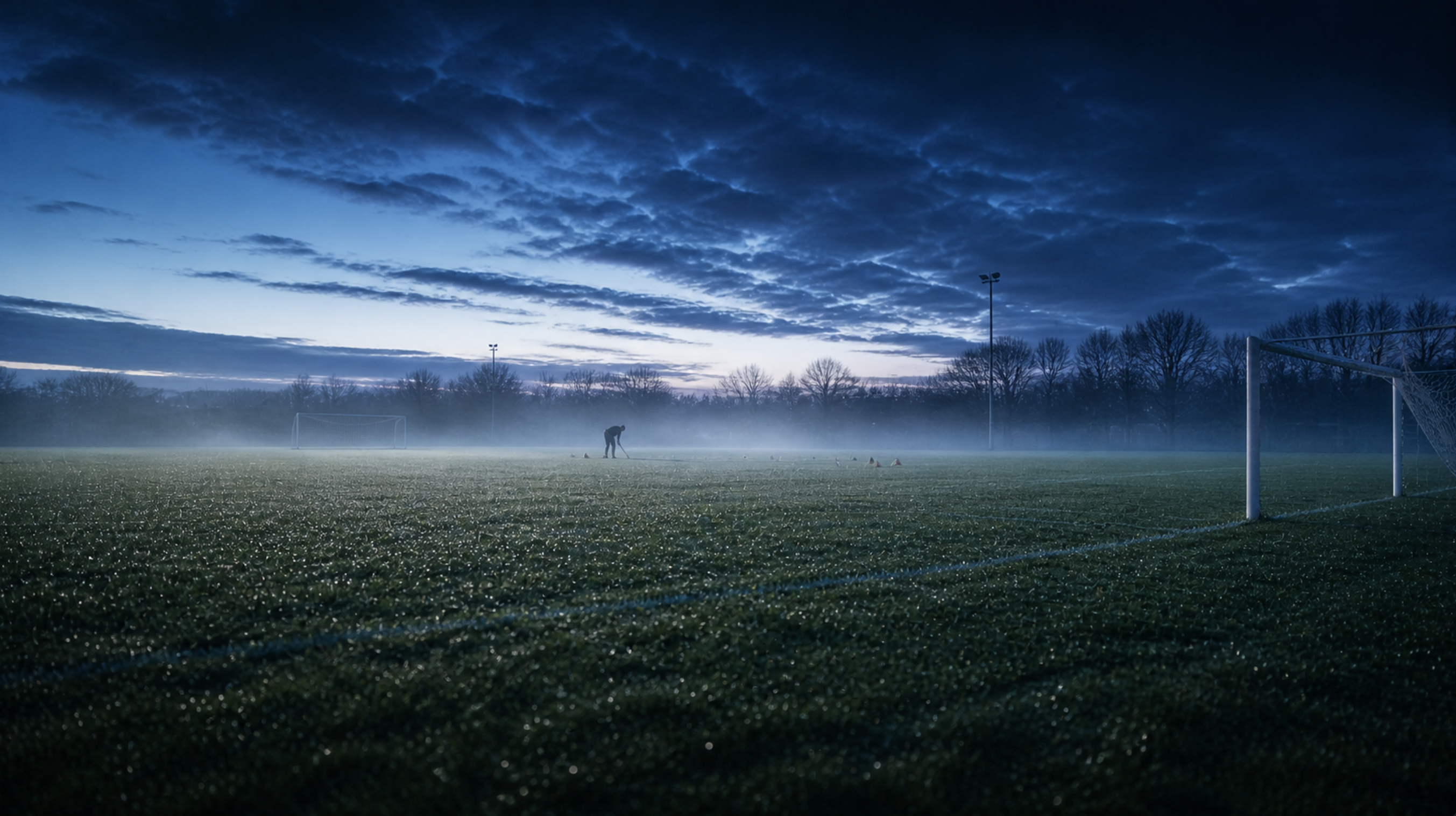 A solitary footballer practising at golden hour, sunset behind.